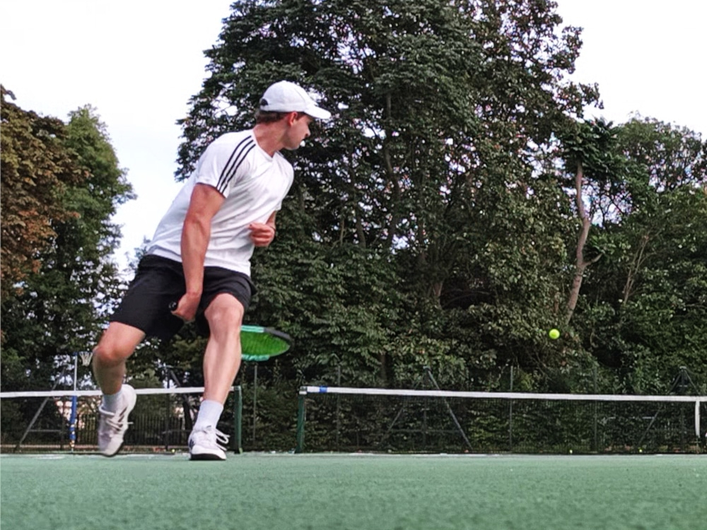 Photograph of Edward Rycroft playing tennis and hitting the ball between his legs.